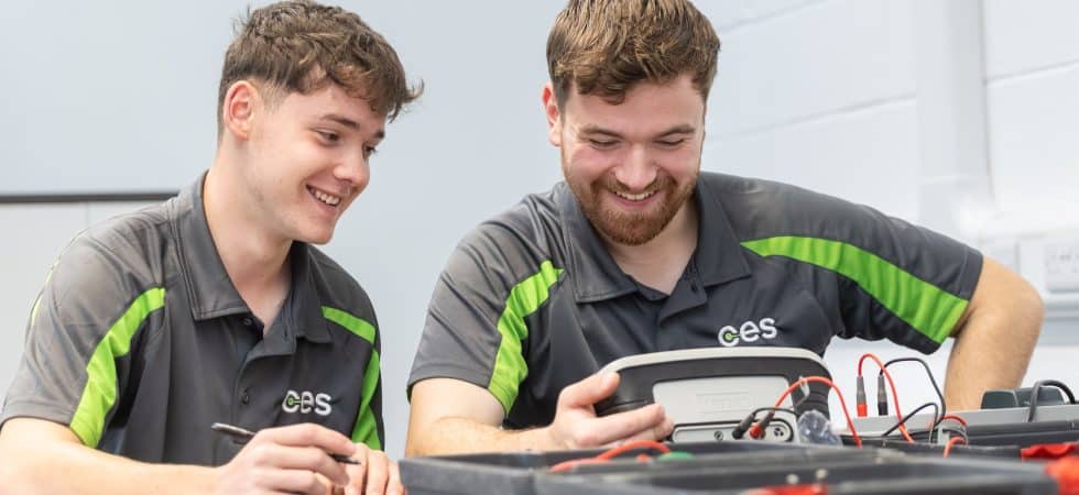 CES apprentices sat at a table, smiling and looking at some electrical equipment.