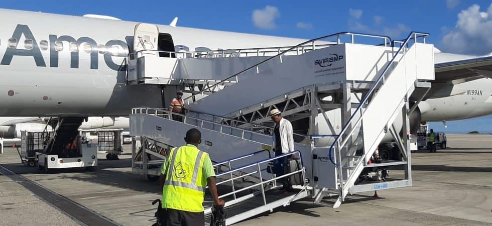 An airport worker pushes a wheelchair towards an Aviramp attached to a passenger plane.