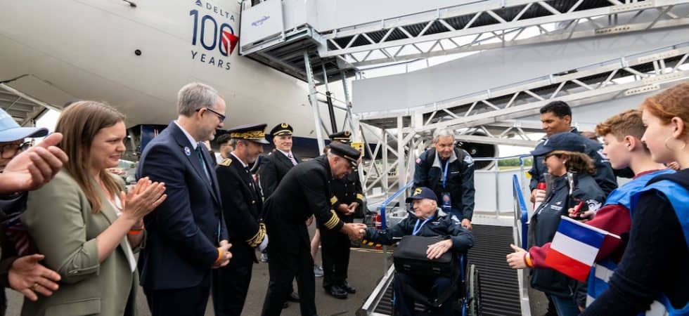 A veteran is escorted down a ramp off an aircraft, waving to a cheering crowd.
