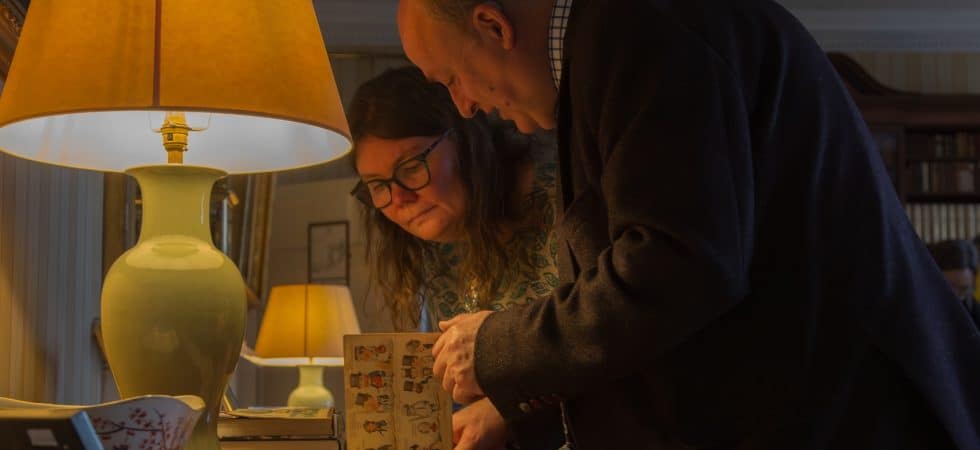 Two people reading through a book in a library of a stately home.